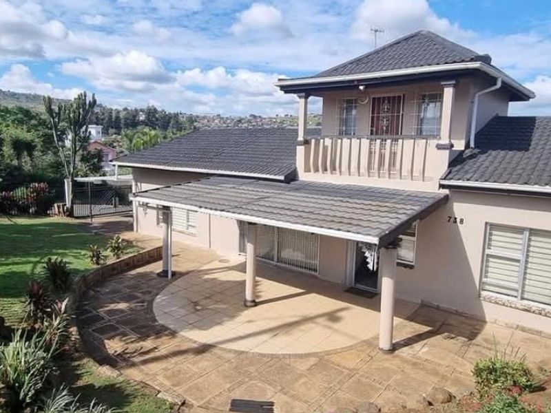 Rear view of a two-story house featuring a covered patio, paved courtyard, upper-level balcony, and landscaped garden area.