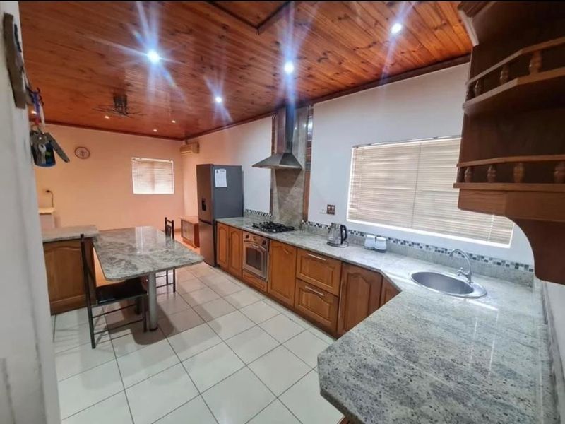 A functional kitchen featuring wooden ceilings, granite countertops, built-in oven, gas hob, and tiled flooring with ample workspace.