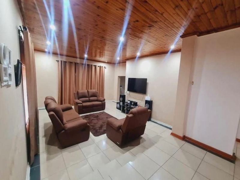Spacious living room featuring a warm timber tongue and groove ceiling, recessed downlighting, and neutral tiled flooring.