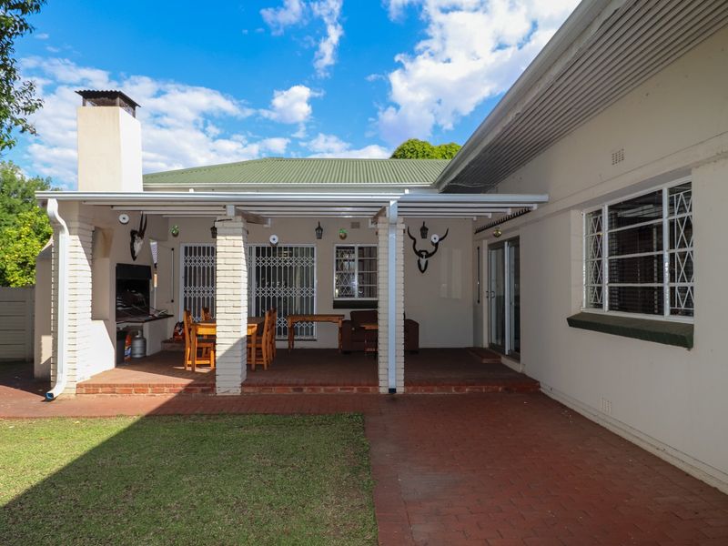 A spacious covered patio featuring a built-in braai, brick paving, and direct access to the rear garden and main house.