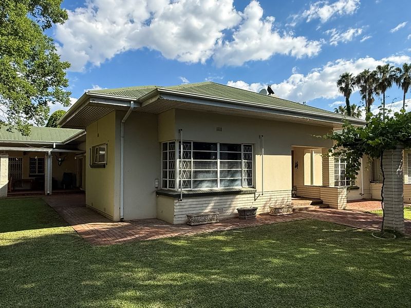 Rear view of the house featuring a metal roof, brick paved patio area, and established garden surroundings.