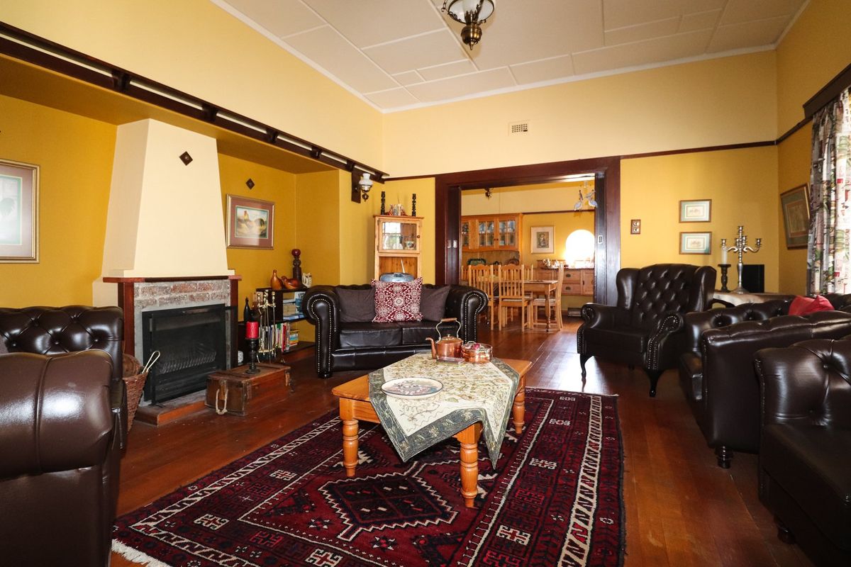 Spacious living room featuring a traditional fireplace with brick hearth, polished timber flooring, and classic architectural details including picture rails and a ceiling rose.
