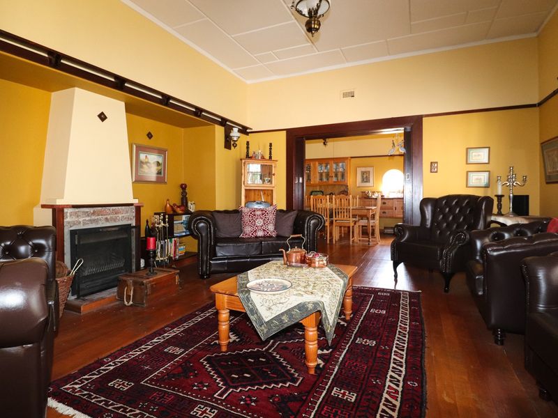 Spacious living room featuring a traditional fireplace with brick hearth, polished timber flooring, and classic architectural details including picture rails and a ceiling rose.
