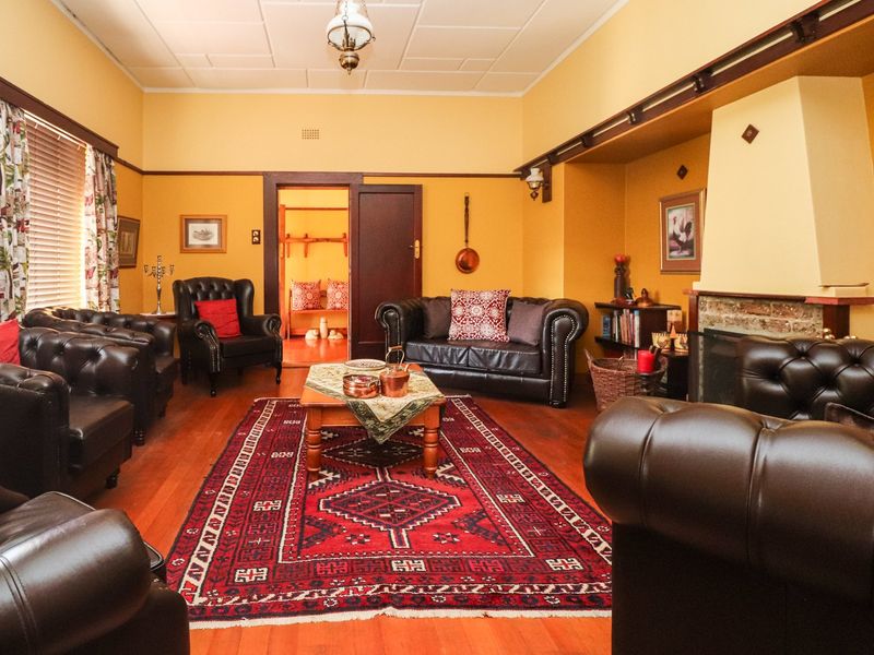 A traditional living room featuring warm yellow walls, timber flooring, and a prominent fireplace, offering a cozy and classic atmosphere.