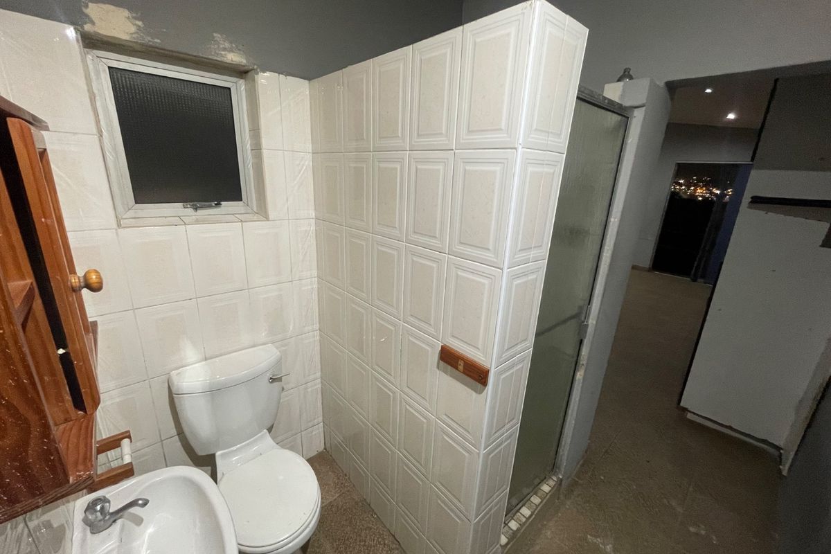 A functional bathroom featuring a pedestal basin, toilet, and a tiled shower enclosure, currently requiring cosmetic updates and finishing touches to the wall surfaces.