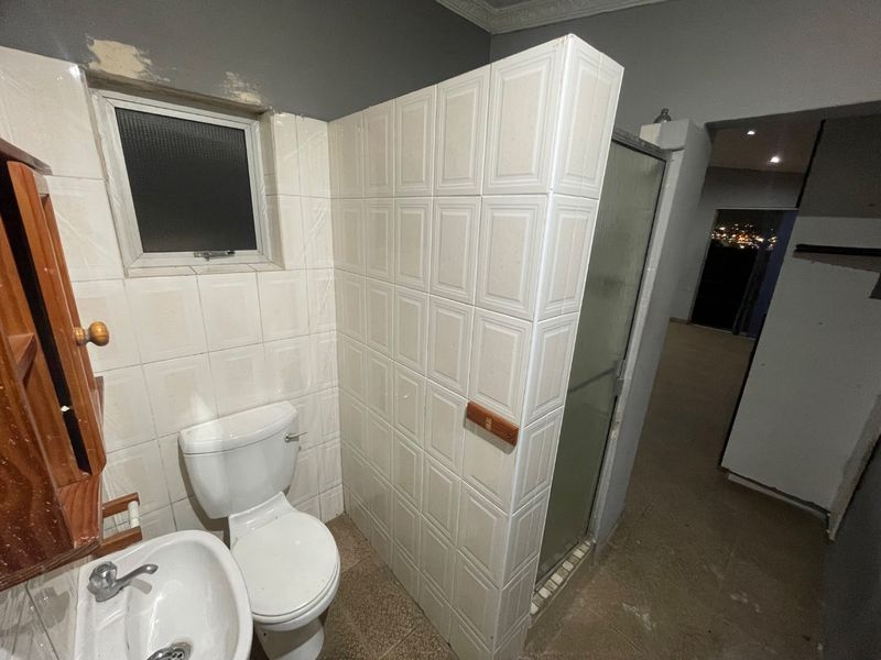 A functional bathroom featuring a pedestal basin, toilet, and a tiled shower enclosure, currently requiring cosmetic updates and finishing touches to the wall surfaces.