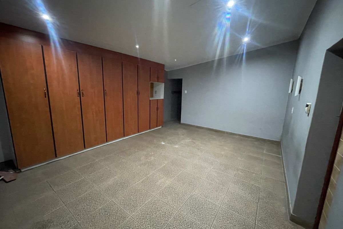 An empty bedroom featuring extensive built-in wooden cupboards, tiled flooring, and recessed ceiling lighting.