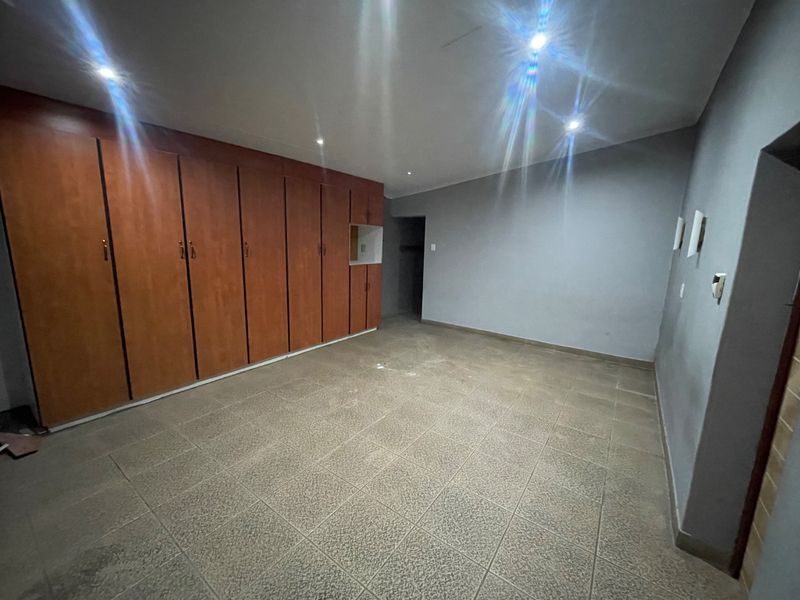 An empty bedroom featuring extensive built-in wooden cupboards, tiled flooring, and recessed ceiling lighting.
