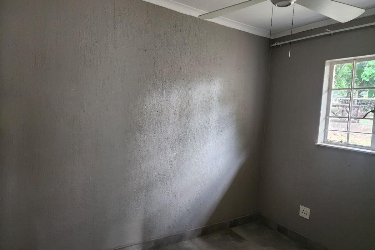 An empty bedroom featuring tiled flooring, a ceiling fan, and a window with security bars, ready for personalization.