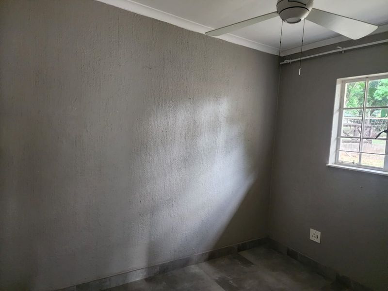 An empty bedroom featuring tiled flooring, a ceiling fan, and a window with security bars, ready for personalization.