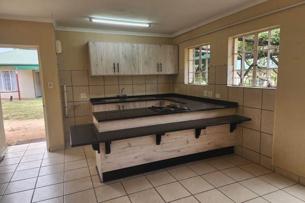 A functional kitchen featuring light wood-grain cabinetry, dark granite countertops, a breakfast bar, and tiled finishes throughout.