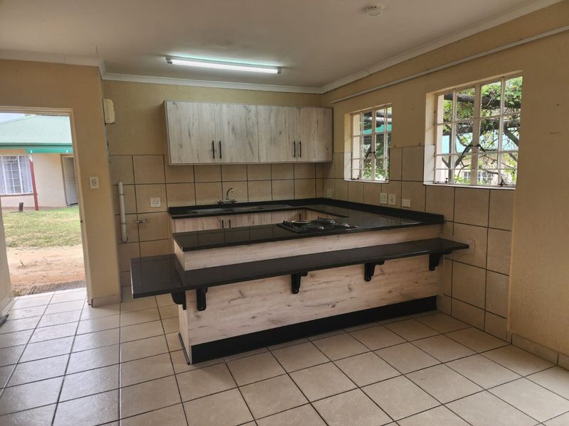 A functional kitchen featuring light wood-grain cabinetry, dark granite countertops, a breakfast bar, and tiled finishes throughout.
