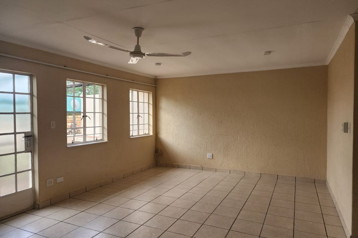 An empty living room featuring tiled flooring, a ceiling fan, and natural light through windows with security bars.