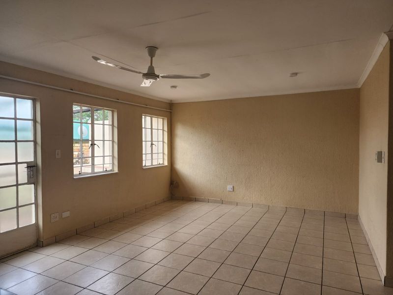 An empty living room featuring tiled flooring, a ceiling fan, and natural light through windows with security bars.