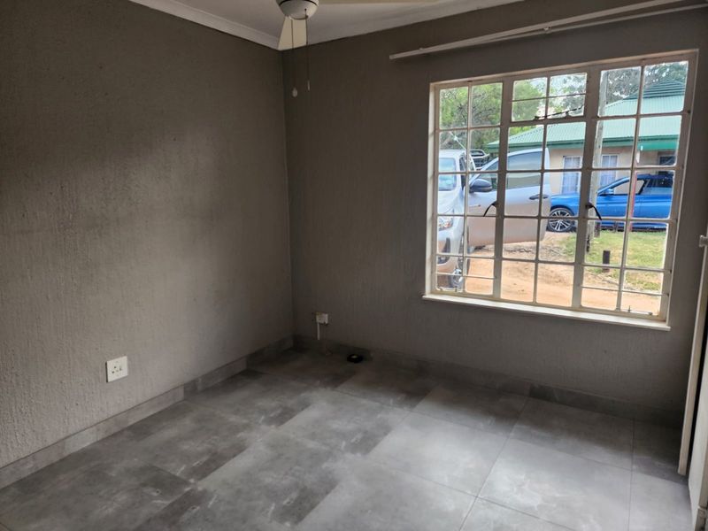 An empty bedroom featuring grey tiled flooring, a ceiling fan, and a window with security bars.