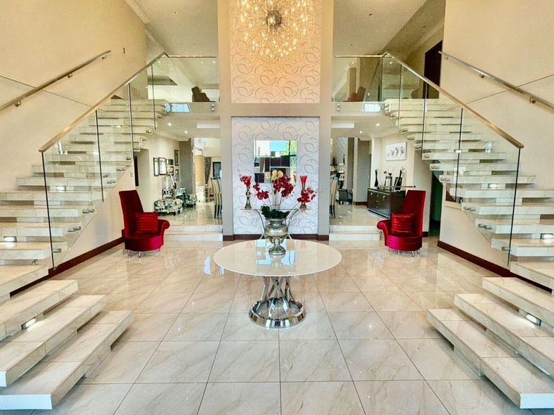 Grand entrance hall featuring dual floating staircases with glass balustrades, polished porcelain flooring, and a striking central feature wall with a chandelier.