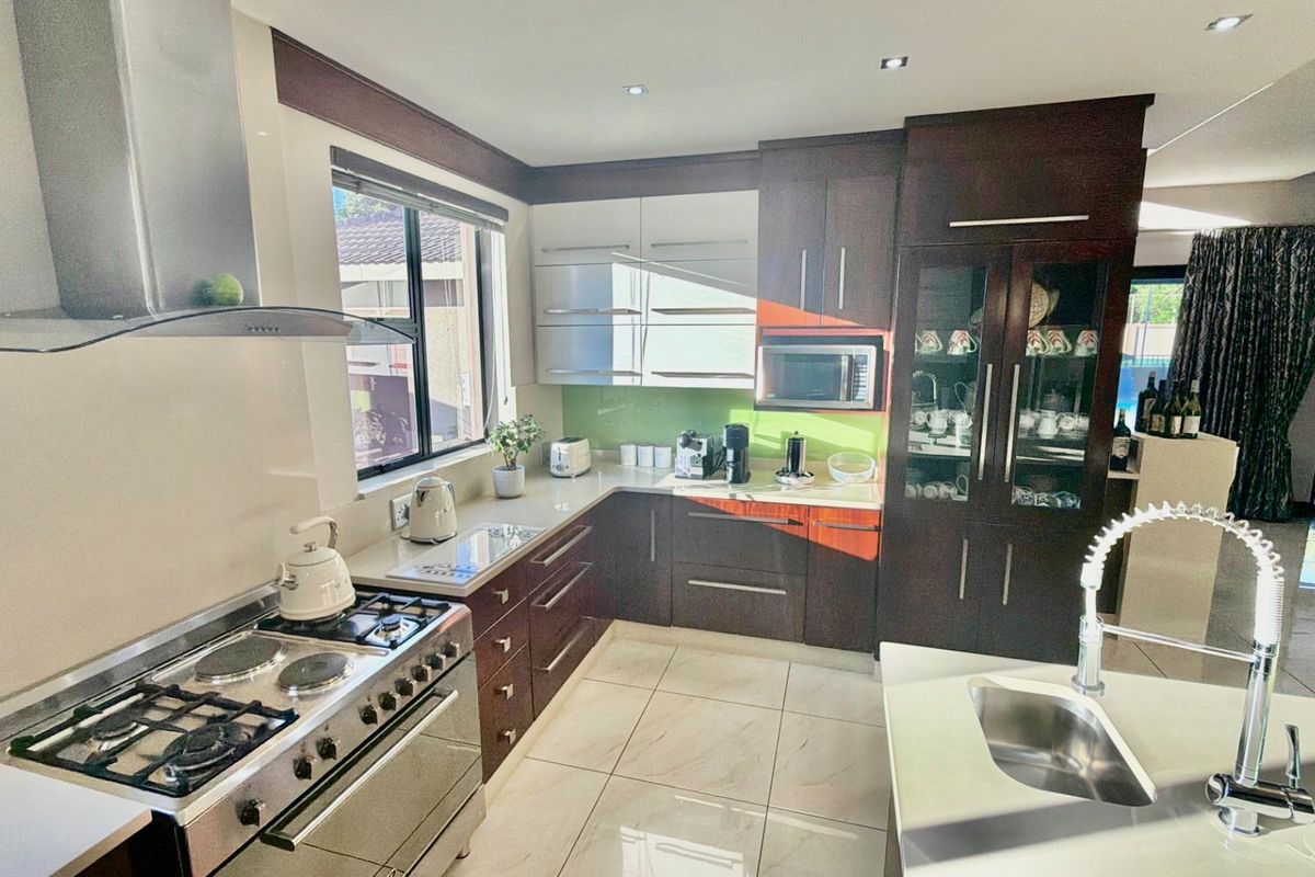 Modern kitchen featuring dark wood cabinetry, a gas stove with extractor, built-in microwave, kitchen island with sink, and tiled flooring.