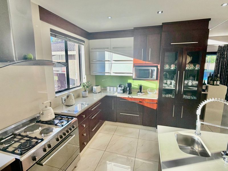 Modern kitchen featuring dark wood cabinetry, a gas stove with extractor, built-in microwave, kitchen island with sink, and tiled flooring.