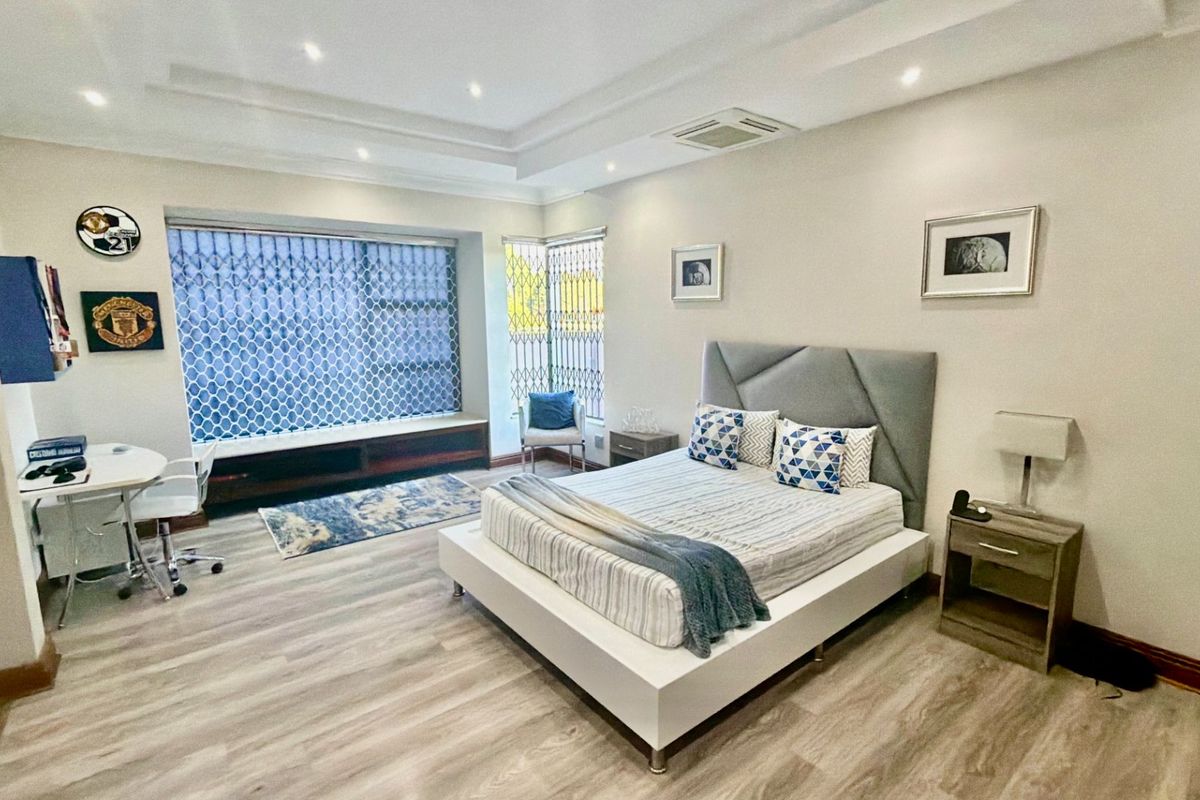 Spacious bedroom featuring modern laminate flooring, a tray ceiling with recessed lighting, integrated air conditioning, and a built-in window seat with security bars.