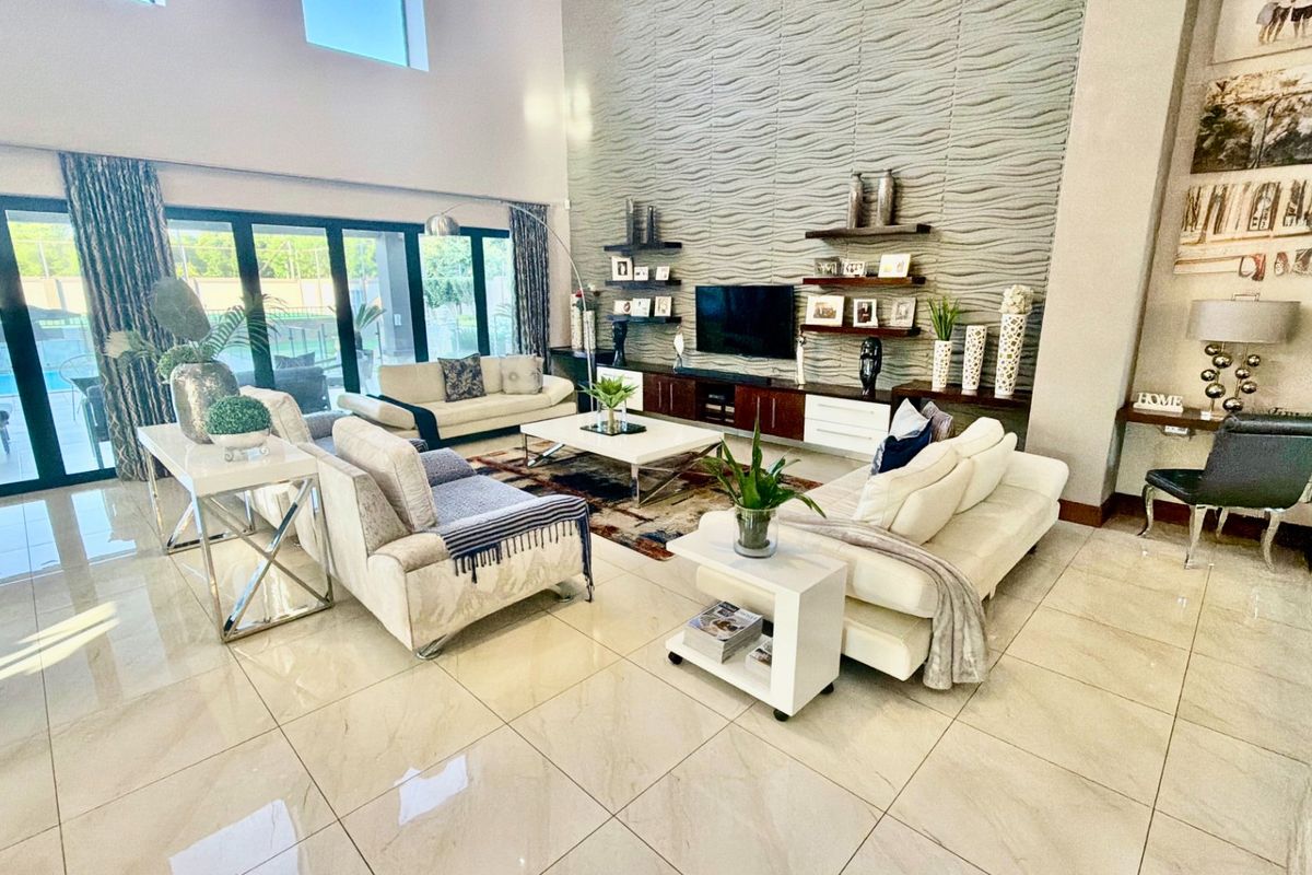 Spacious double-volume living room featuring large format floor tiles, a striking textured feature wall with built-in cabinetry, and expansive sliding doors leading outdoors.