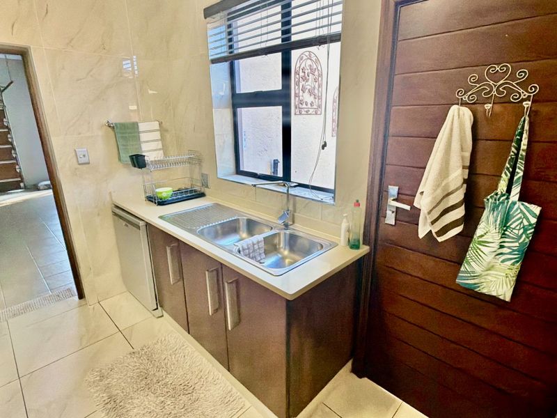 A functional scullery area featuring built-in cabinetry, a double bowl stainless steel sink, and tiled finishes throughout.