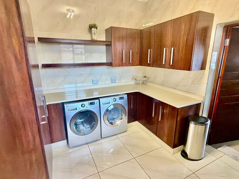 A modern, well-appointed laundry room featuring sleek dark wood cabinetry, stone countertops, and polished tile flooring with a clean, contemporary finish.