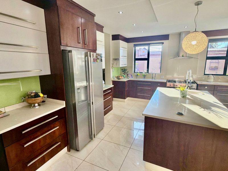 Modern kitchen featuring dark wood cabinetry, stone countertops, a central island, and high-quality stainless steel appliances with ample natural light.