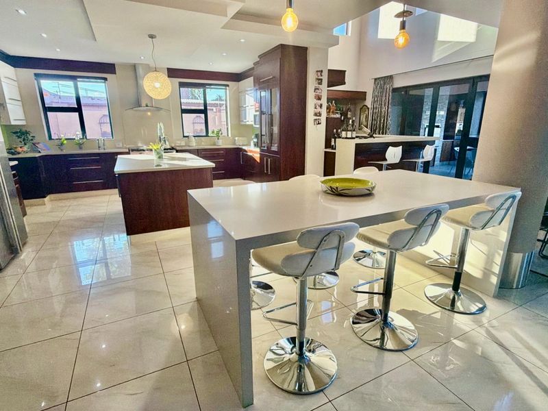 Spacious open-plan kitchen featuring a large central island, breakfast bar, modern cabinetry, and high-gloss tiled flooring, seamlessly flowing into the dining area.
