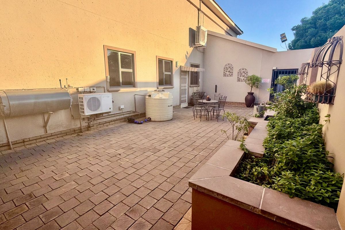 A paved rear courtyard featuring a raised brick planter, water storage tank, and exterior utility installations including a solar geyser and air conditioning unit.