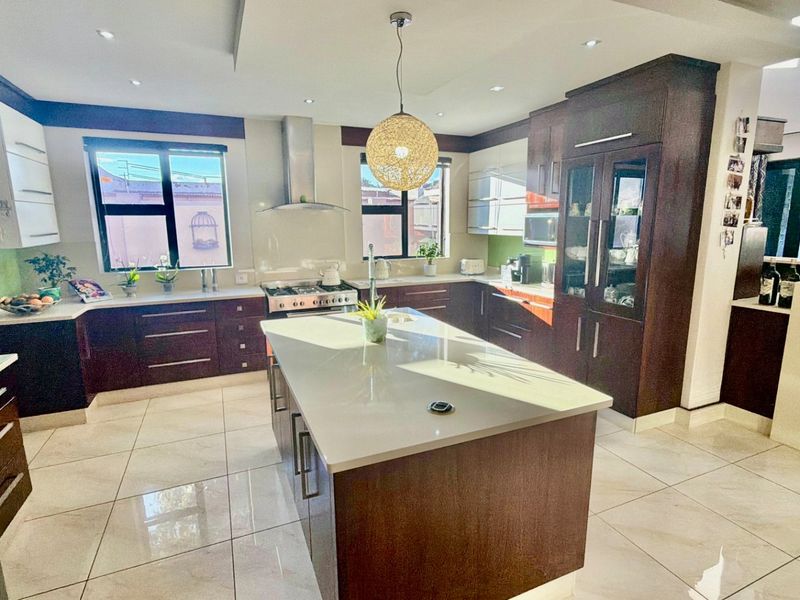 Modern kitchen featuring a central island with stone countertops, dark wood cabinetry, gas hob, integrated appliances, and polished tiled flooring.