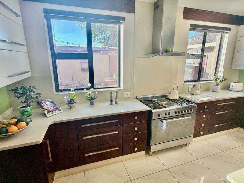 Modern kitchen featuring dark wood cabinetry, light quartz countertops, gas stove with stainless steel extractor, and tiled flooring with ample natural light.
