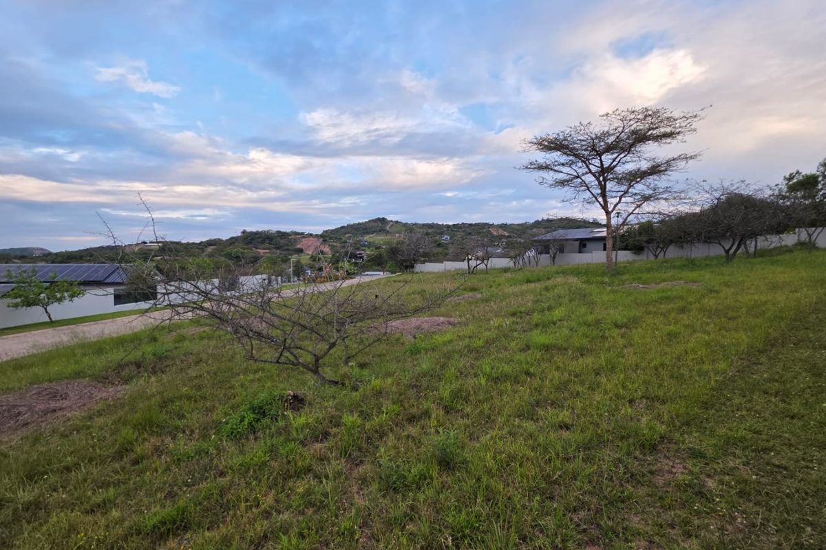 A vacant residential plot featuring established grass and perimeter walling, offering a scenic view of the surrounding landscape.