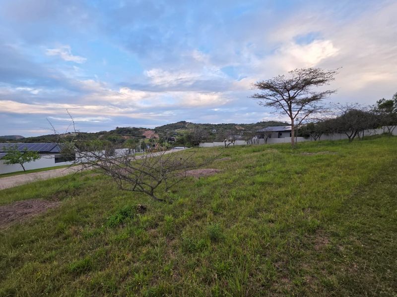 A vacant residential plot featuring established grass and perimeter walling, offering a scenic view of the surrounding landscape.