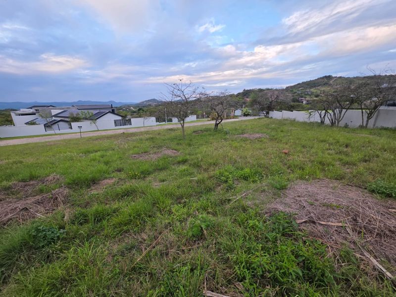 A vacant residential plot featuring natural grass cover, perimeter boundary walls, and views of the surrounding landscape and neighboring properties.