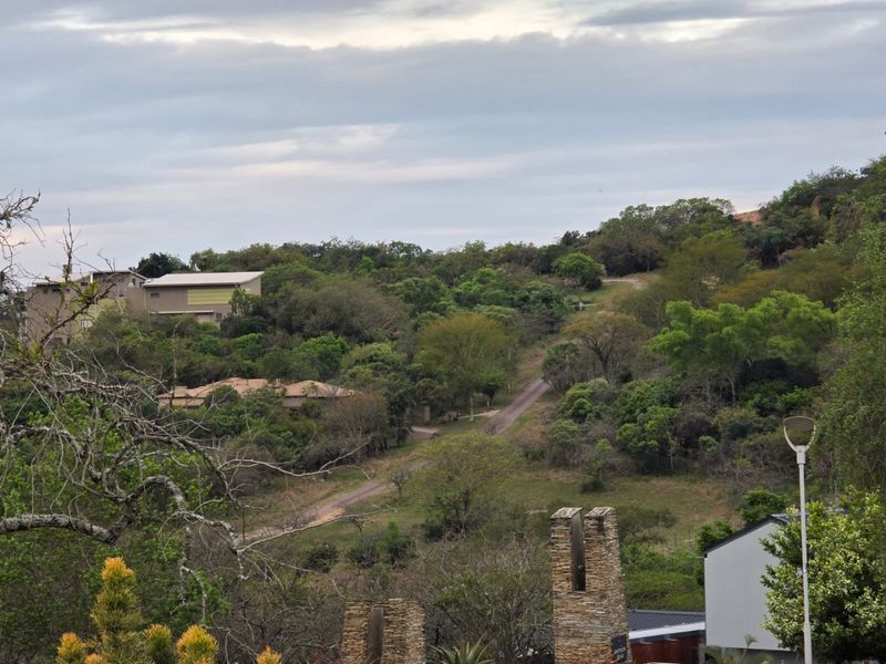 A scenic view of the surrounding natural landscape, featuring rolling hills, lush greenery, and established trees within the residential estate.