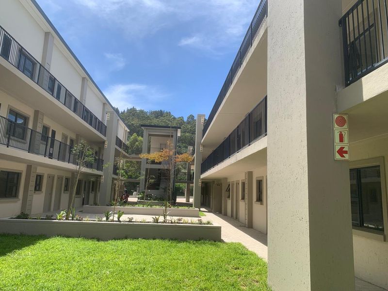 A well-maintained apartment complex courtyard featuring paved walkways, landscaped garden beds, and modern metal balustrades on the upper levels.