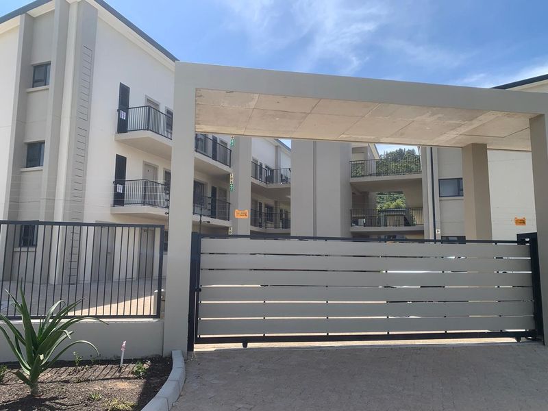 Modern apartment complex entrance featuring a secure automated sliding gate, concrete portal, and multi-level building facade with private balconies.