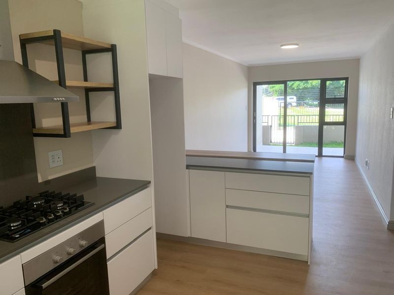 Modern open-plan kitchen and living area featuring sleek white cabinetry, stone countertops, built-in appliances, and direct access to an outdoor patio through sliding doors.