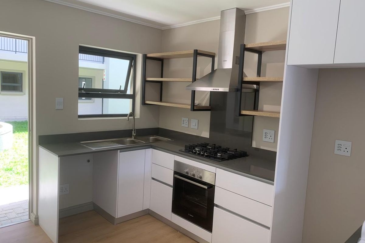 Modern kitchen featuring white cabinetry, stone countertops, built-in oven, gas hob, extractor fan, and open shelving with direct access to the exterior.