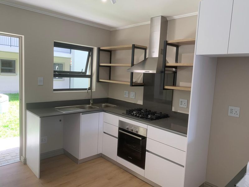 Modern kitchen featuring white cabinetry, stone countertops, built-in oven, gas hob, extractor fan, and open shelving with direct access to the exterior.