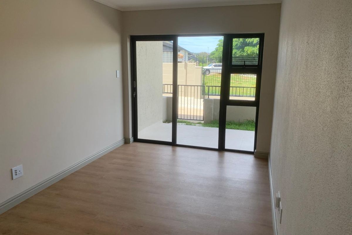 A bright, empty bedroom featuring modern laminate flooring and a large sliding glass door that provides direct access to an outdoor patio area.