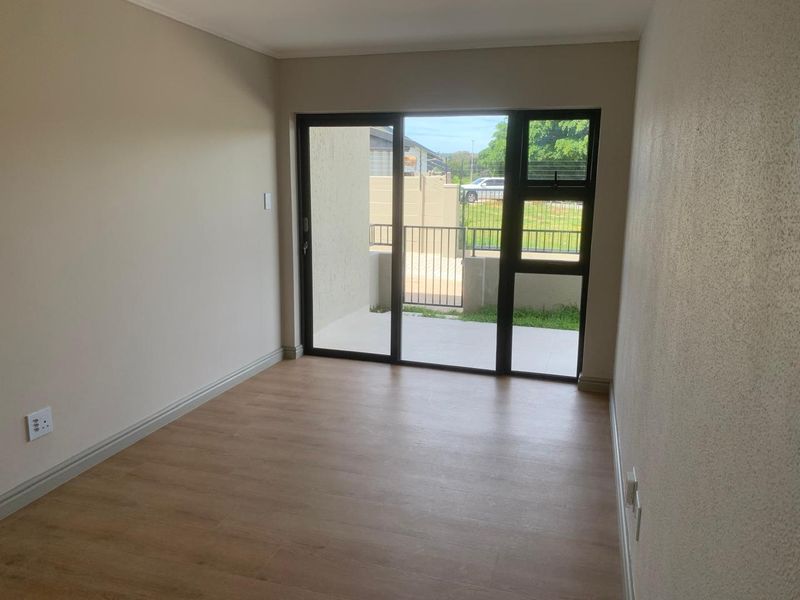 A bright, empty bedroom featuring modern laminate flooring and a large sliding glass door that provides direct access to an outdoor patio area.