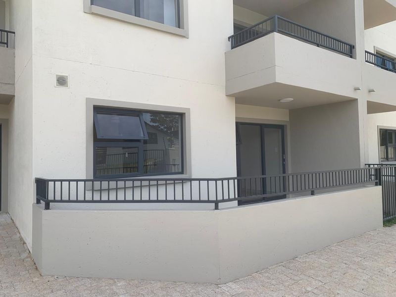 Exterior view of an apartment building featuring a ground-floor patio with metal railings, sliding glass doors, and modern casement windows.