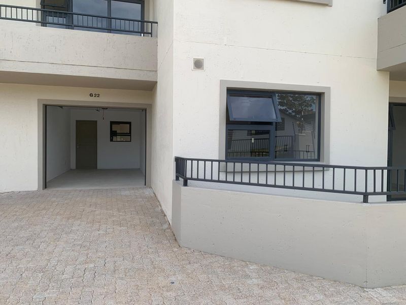 Exterior view of an apartment building featuring a paved driveway, garage entrance, and modern aluminium window frames with a metal balustrade.