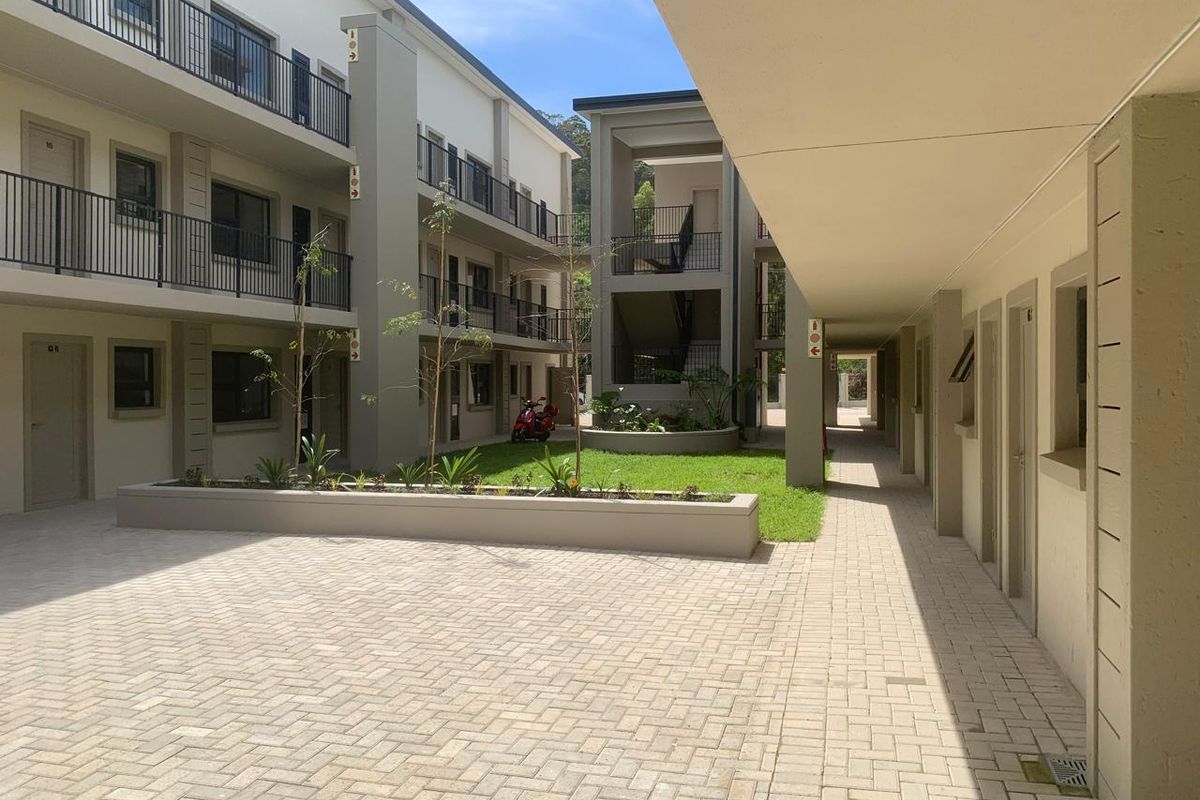A well-maintained apartment complex courtyard featuring paved walkways, landscaped garden beds, and multi-level access balconies.