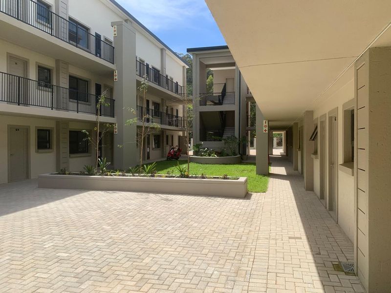A well-maintained apartment complex courtyard featuring paved walkways, landscaped garden beds, and multi-level access balconies.