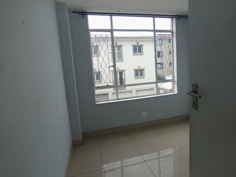 A bright, empty bedroom featuring neutral tiled flooring and a large window with security bars, offering a clean and versatile living space.