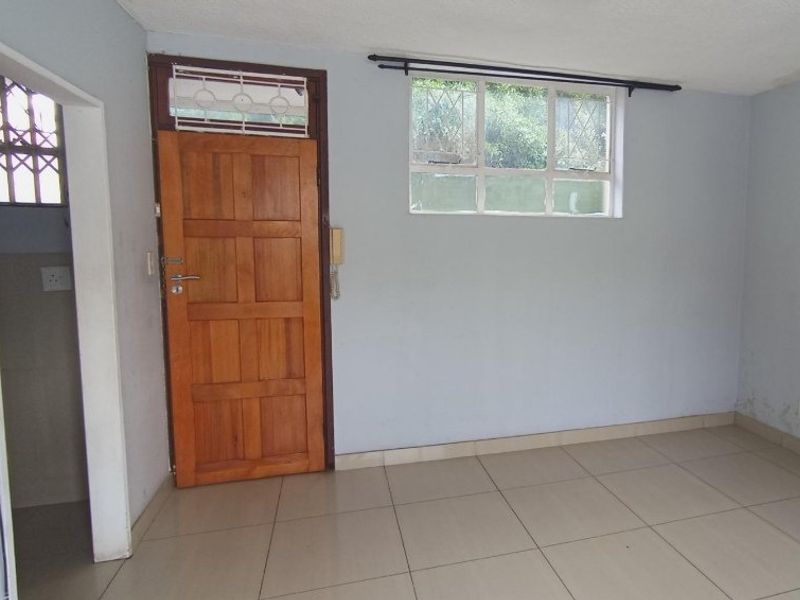 An empty living area featuring tiled flooring, a wooden entrance door with security gate, and a window with security bars.