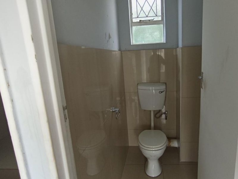 A small, functional bathroom featuring a standard toilet, tiled walls and flooring, and a window with security bars.