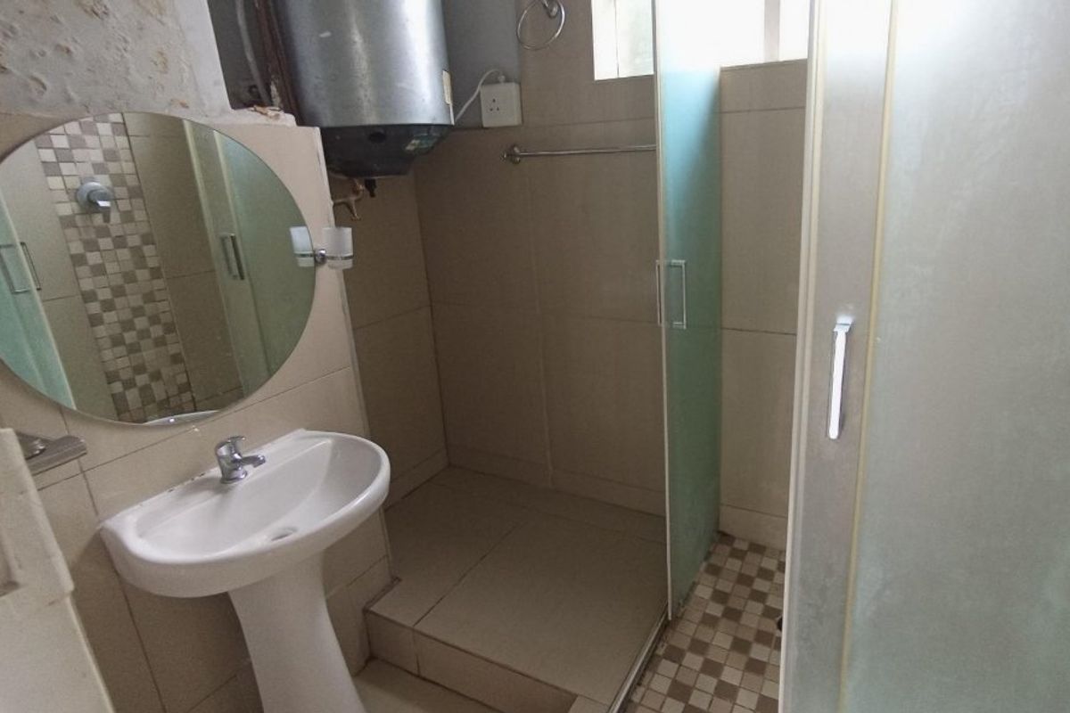 A compact bathroom featuring a pedestal basin, shower enclosure, and tiled finishes. The space includes an exposed electric geyser and requires minor cosmetic finishing.